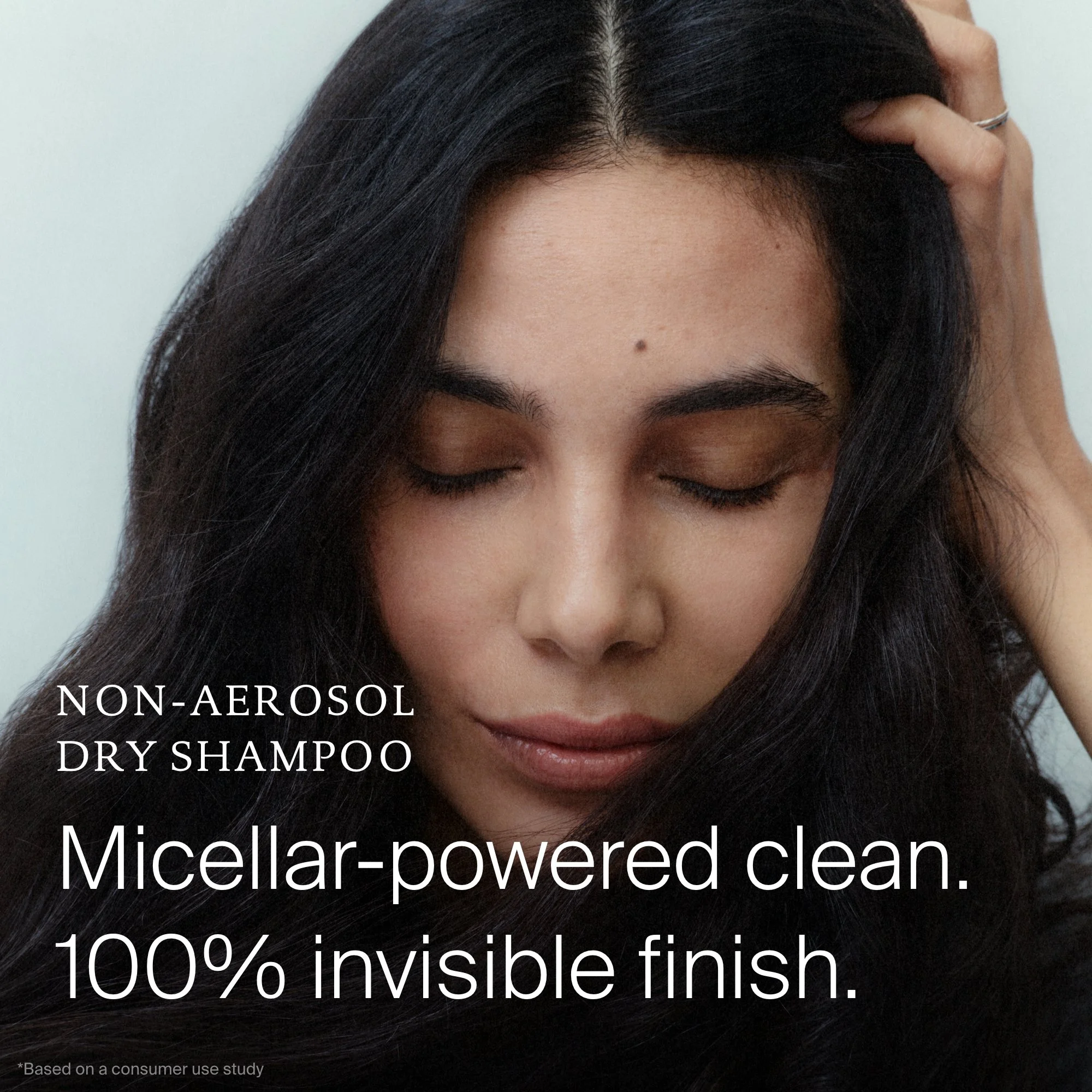 A woman with dark hair is gently touching her scalp with one hand, and her eyes are closed. The image promotes non-aerosol, dry shampoo with a micellar-powered clean, highlighting 100% invisible finish, as seen in the text overlay.
