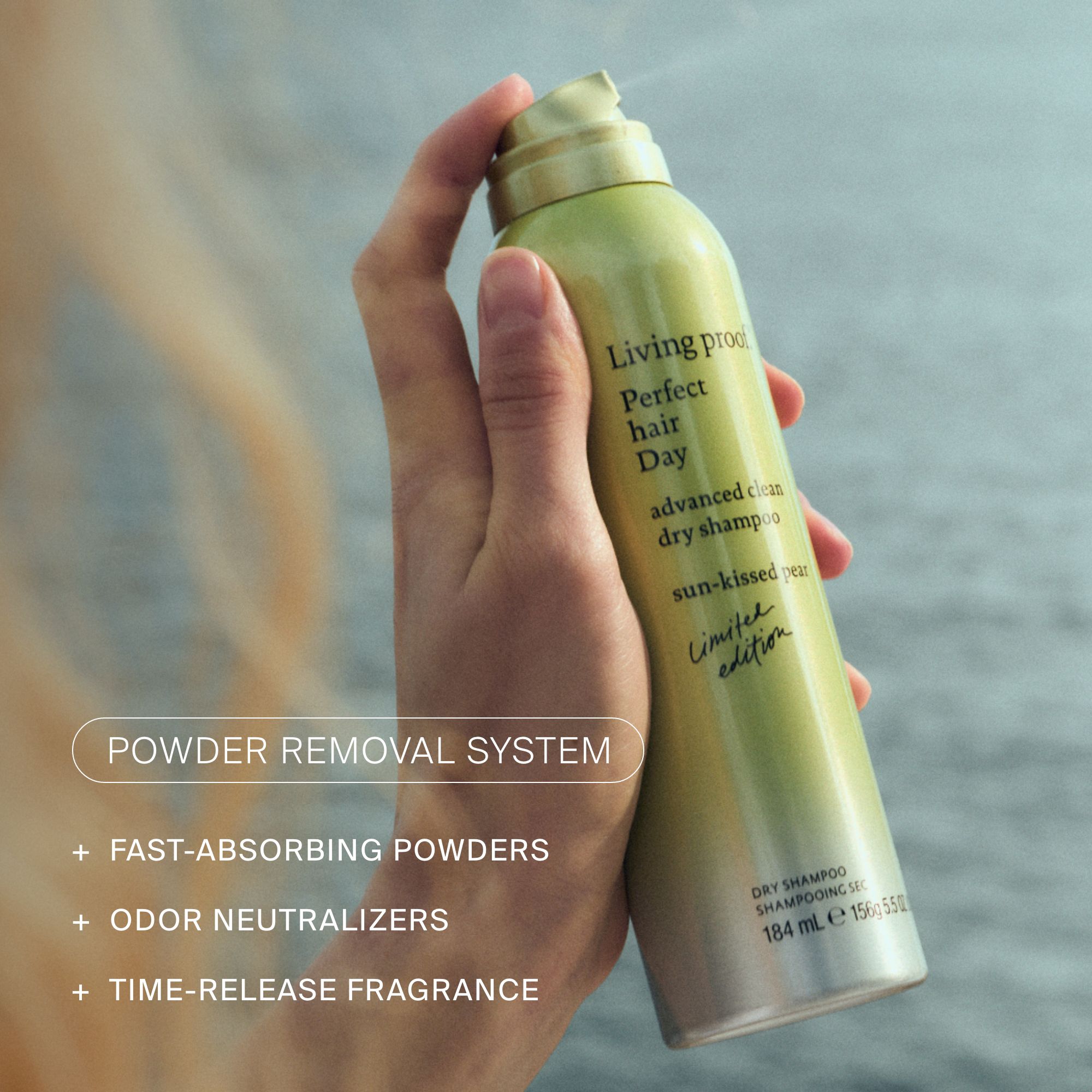 A hand holding a green and gold can of dry shampoo. The can has text indicating it is a powder removal system for fast-absorbing powders, odor neutralizers, and time-release fragrances.