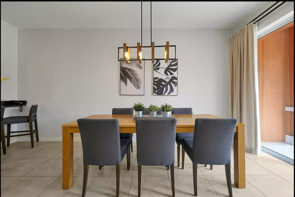 Dining room with a wooden table, six gray chairs, minimalist wall art, chandelier, and sliding glass door with curtains.
