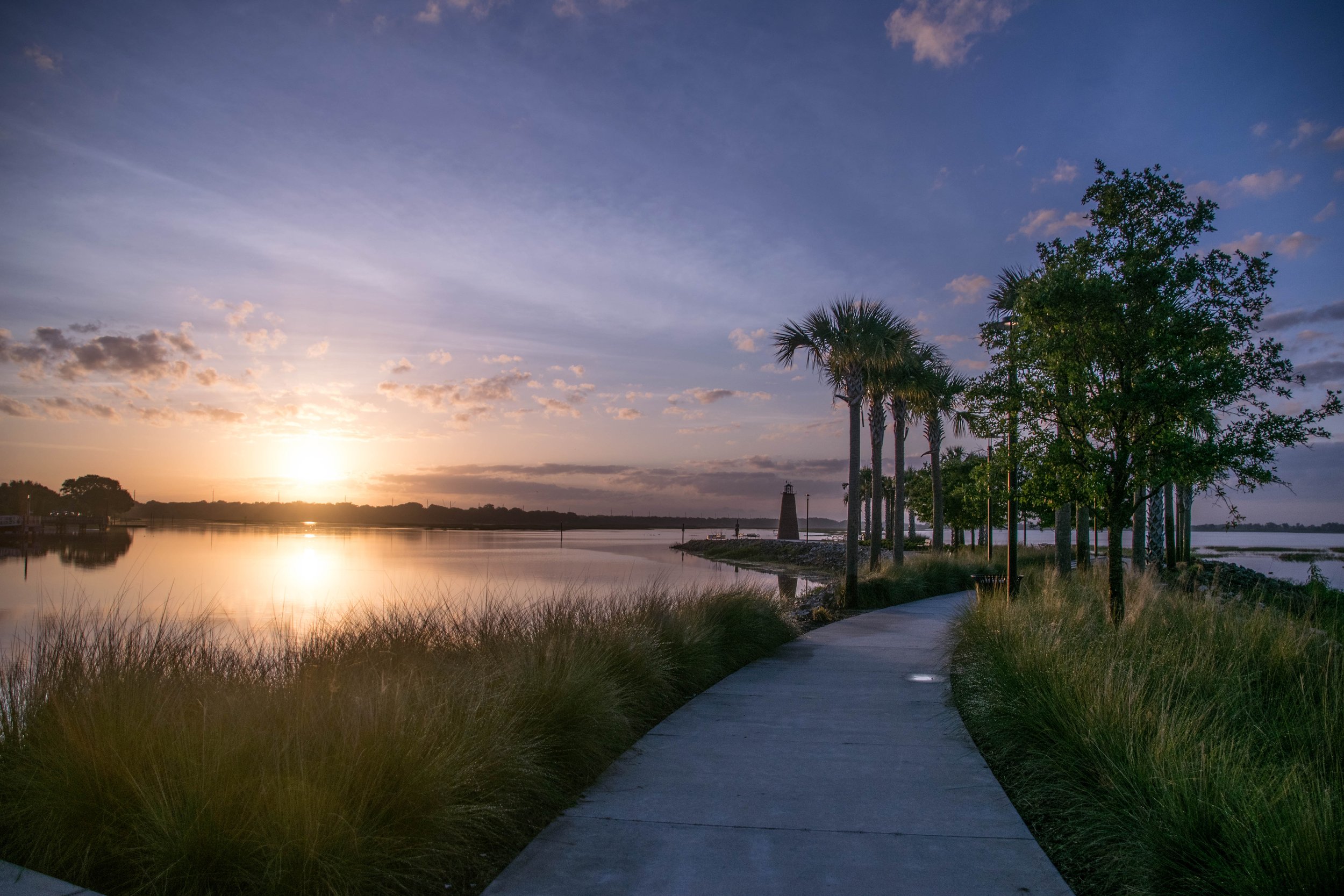 Sunset along Lake Tohopekaliga at Kissimmee Lakefront Park with a waterfront path and trees.