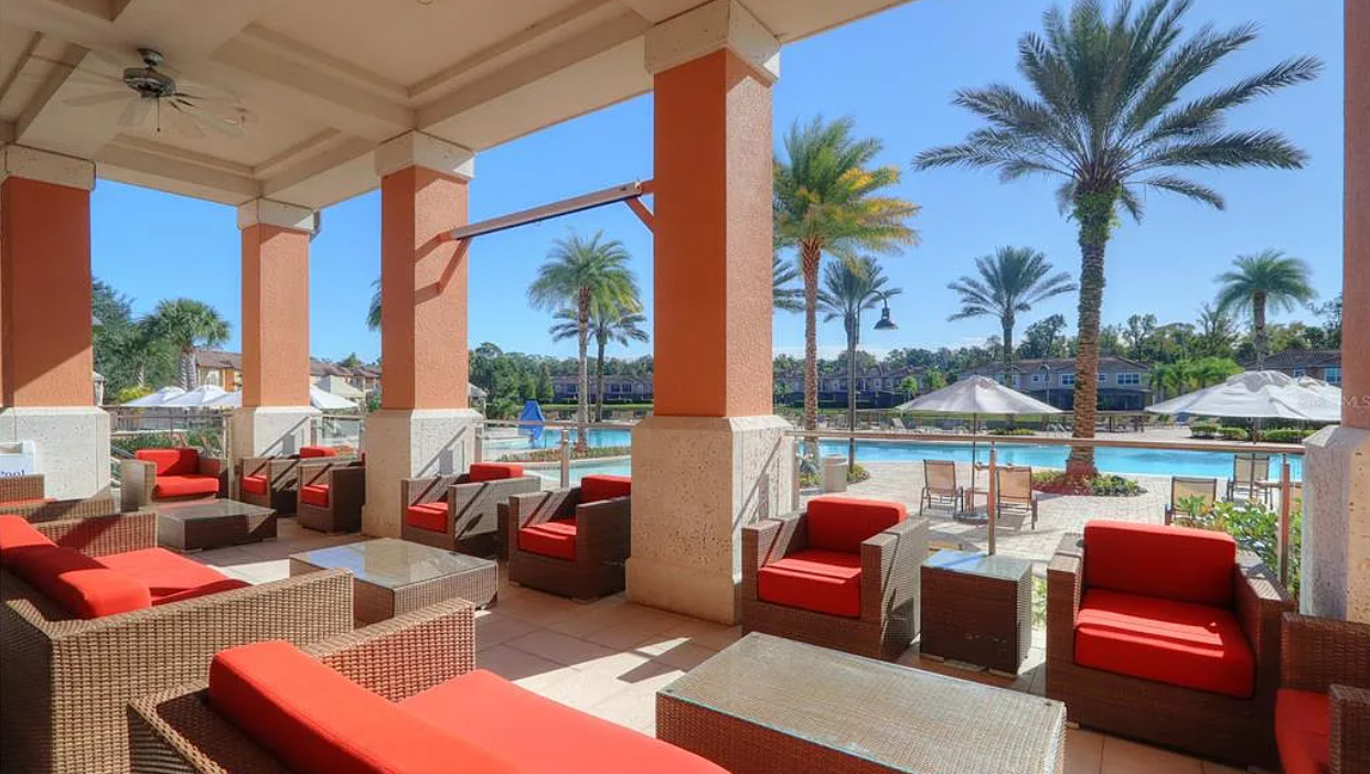 Outdoor pool area with lounge chairs and umbrellas, surrounded by palm trees under a clear blue sky.