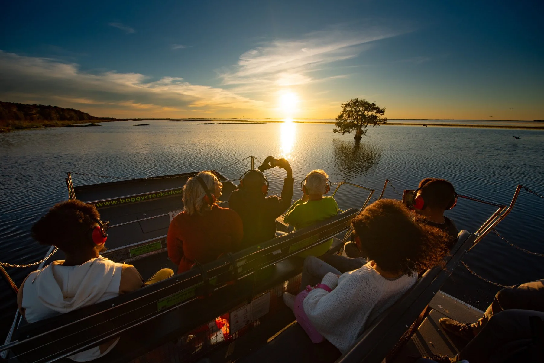 Passengers riding an airboat through Central Florida wetlands at sunset.