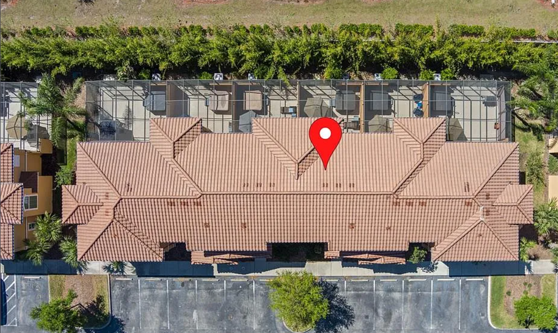 Aerial view of a building with a red tile roof, surrounded by parking lot, trees, and landscaped areas.