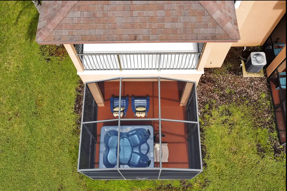 A backyard enclosed porch with a hot tub, two chairs, and a small table.