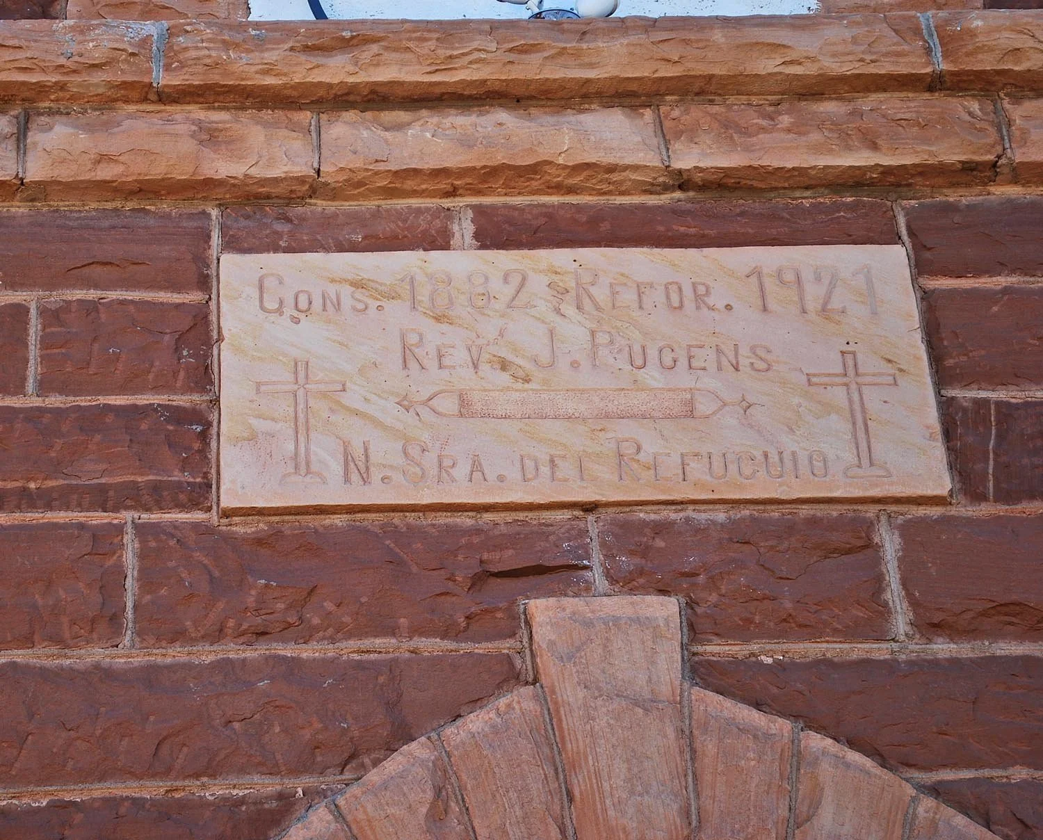 A stone plaque on a brick wall inscribed with historical information, featuring crosses and an arrow.