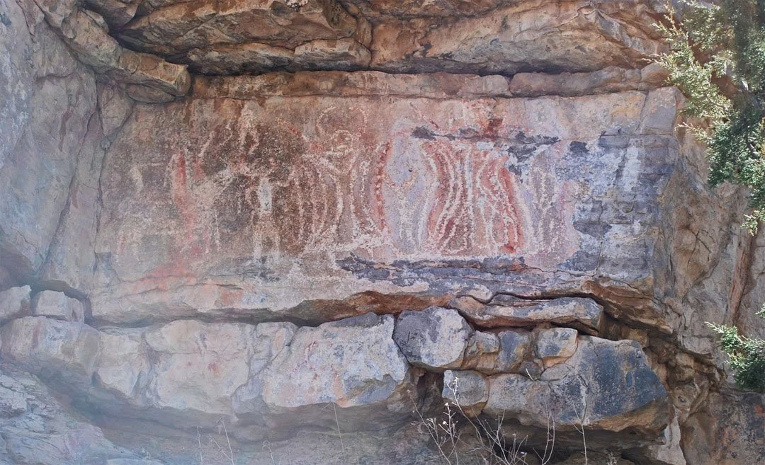 Ancient rock painting of abstract or possibly bison figures on a cliff face.