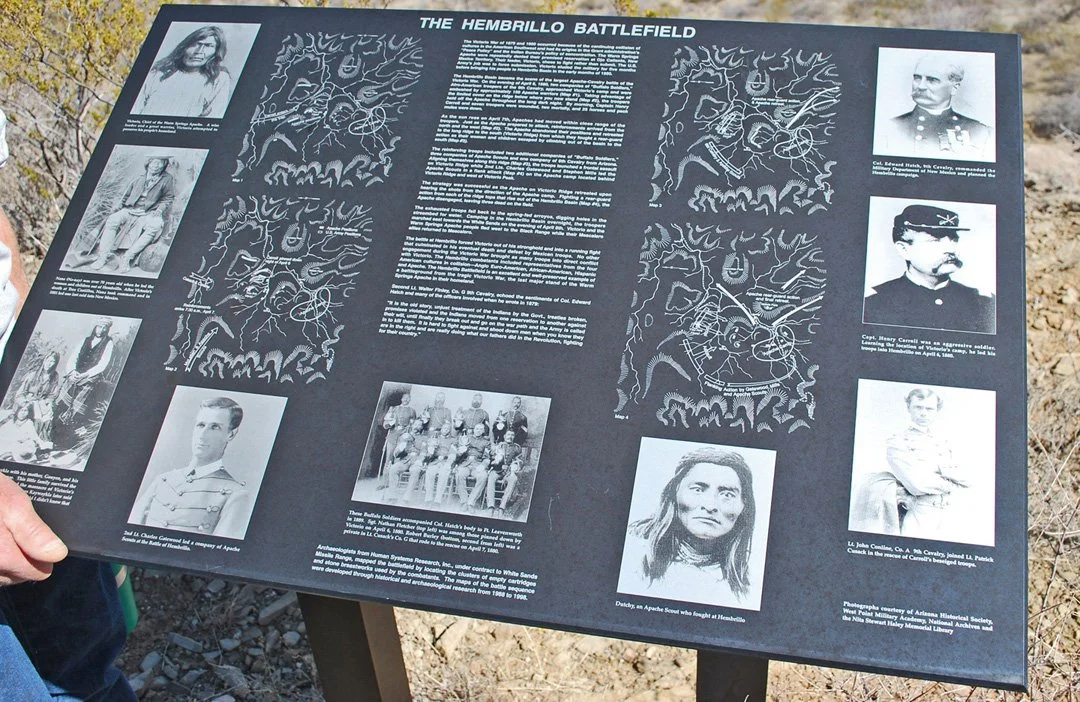 Historical information board titled 'The Hembrillo Battlefield' with black and white photographs of soldiers, Native Americans, and historical figures, along with diagrams of the battlefield layout.