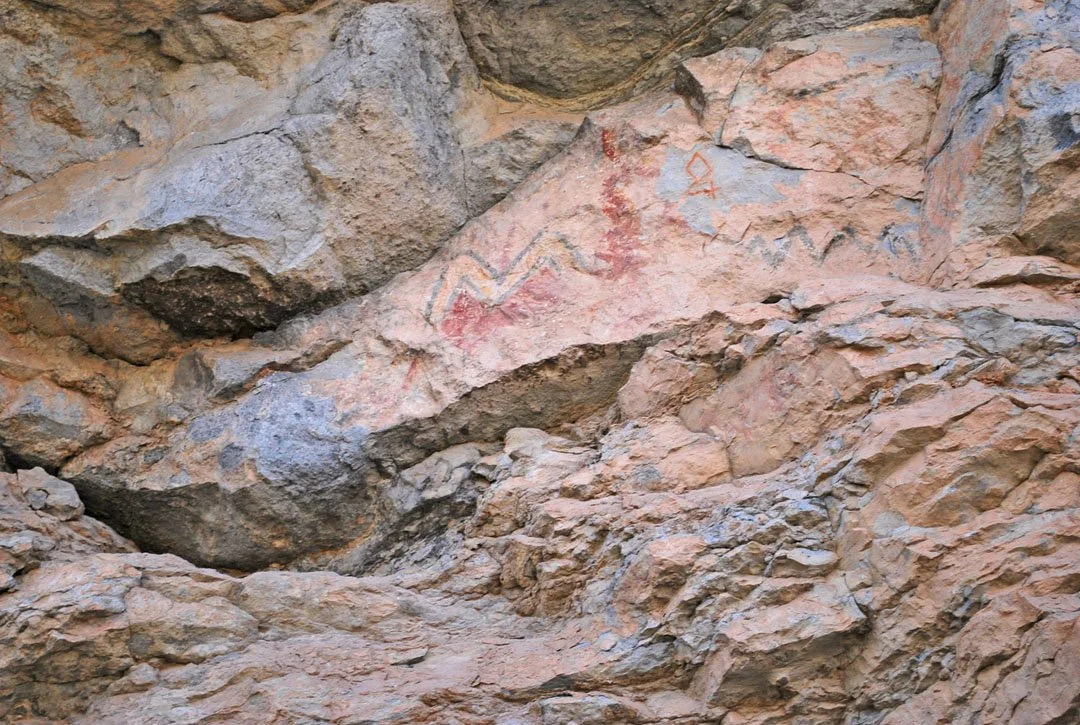 Ancient rock wall with painted red and yellow zigzag and geometric designs.