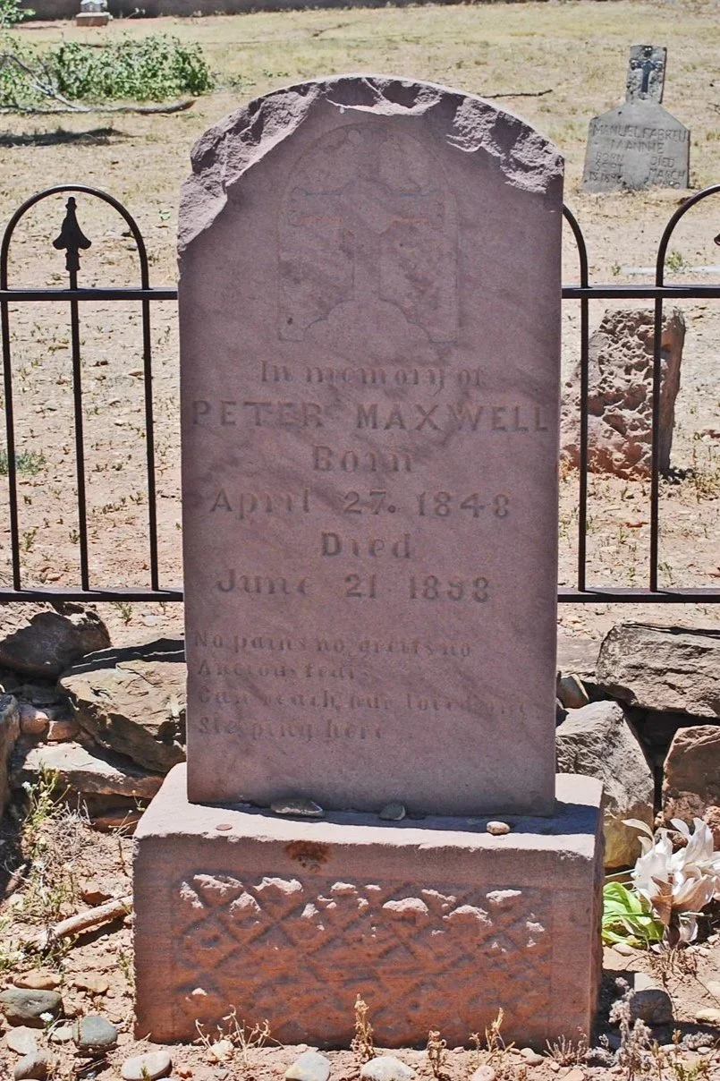 A tombstone for Peter Maxwell, born April 27, 1848, died June 21, 1858, in a cemetery with other gravestones and a small fence.