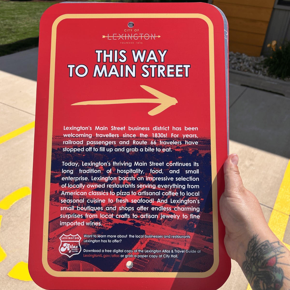 A red and beige informational sign with an arrow pointing right, indicating the way to Main Street in Lexington, Alabama. The sign provides details about Lexington's Main Street business district and encourages learning more about local businesses and restaurants.