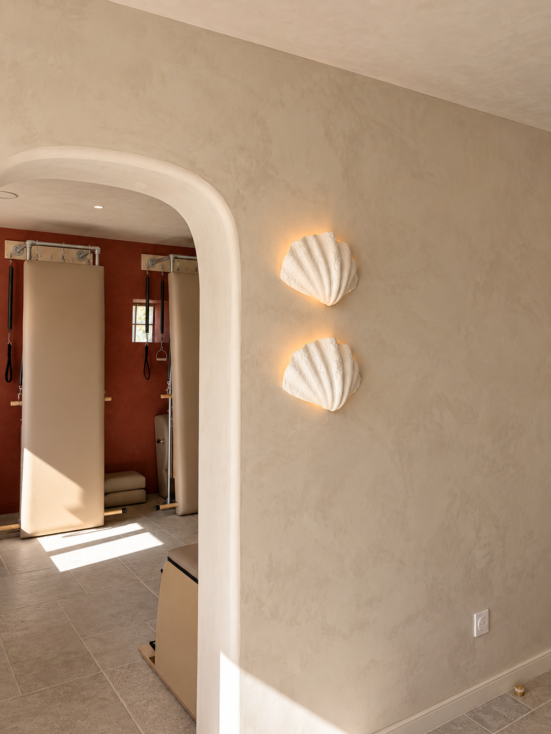Mur beige avec deux coquillages en relief éclairés par une lumière douce.
