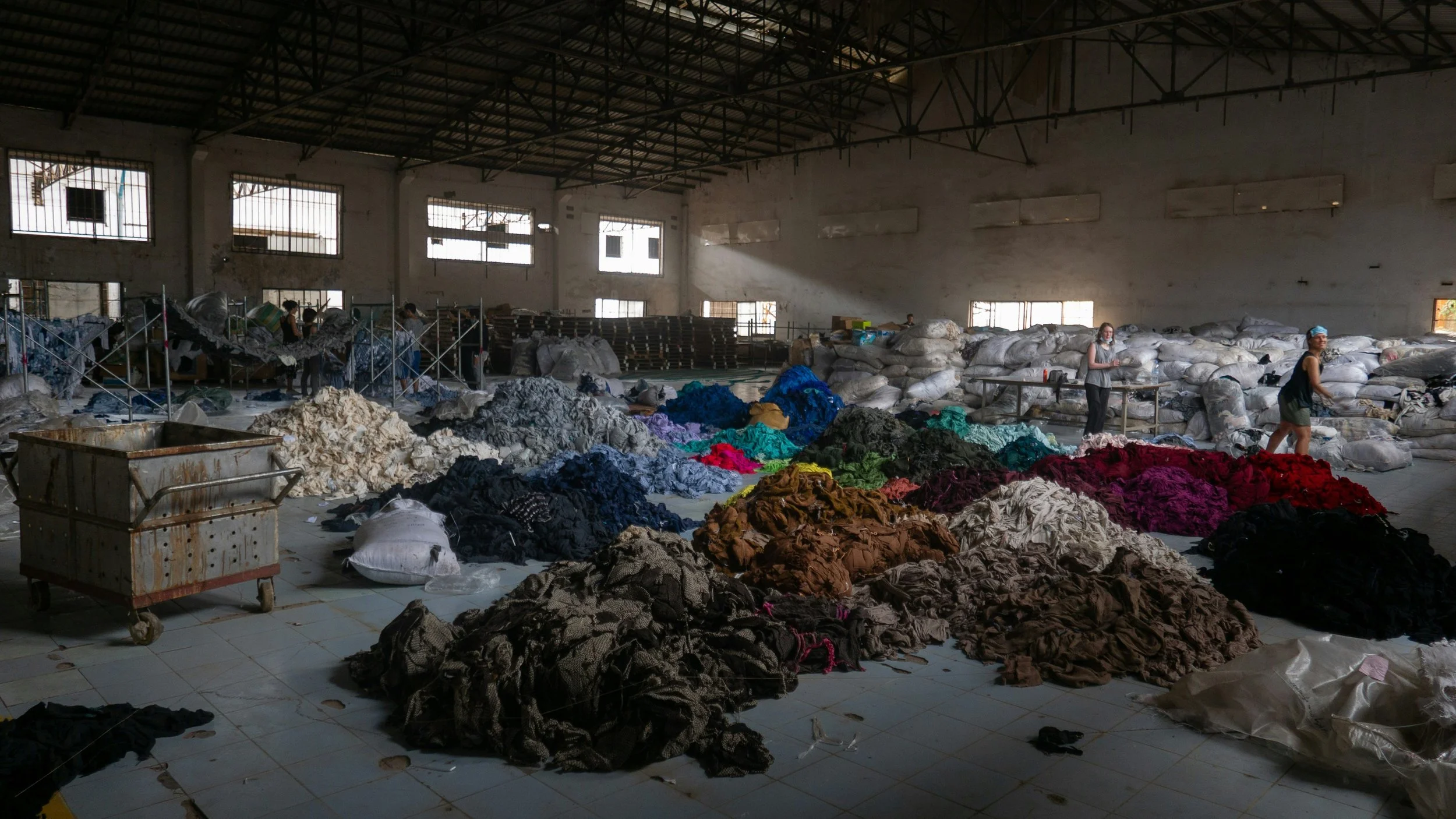 Large sorted piles of discarded colorful clothing and fabric in a warehouse.