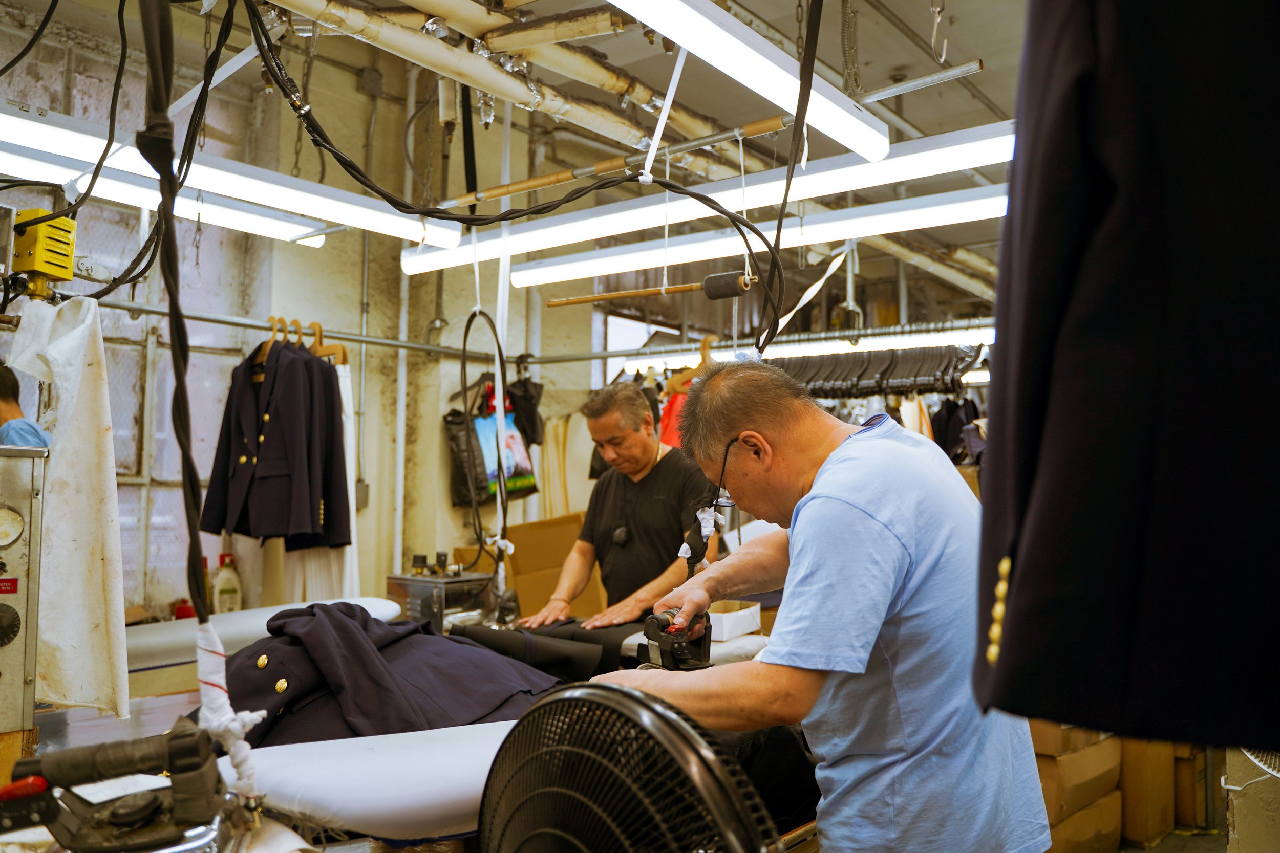 Two garment workers pressing and finishing clothing items in a factory.
