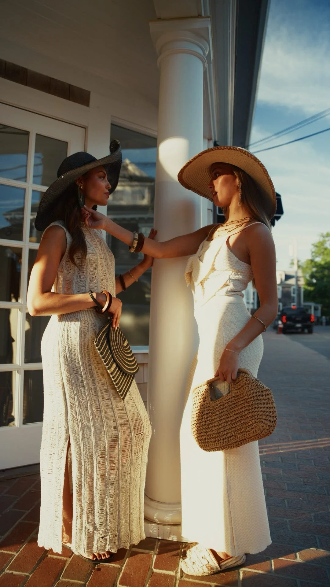 Two women in long dresses and wide brimmed hats standing outside a shop