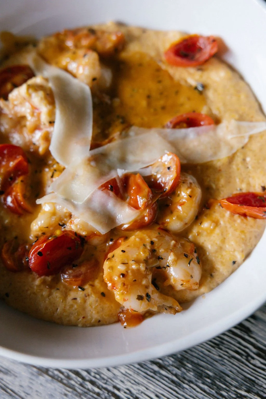 Shrimp and cherry tomato dish topped with shaved cheese in a white bowl