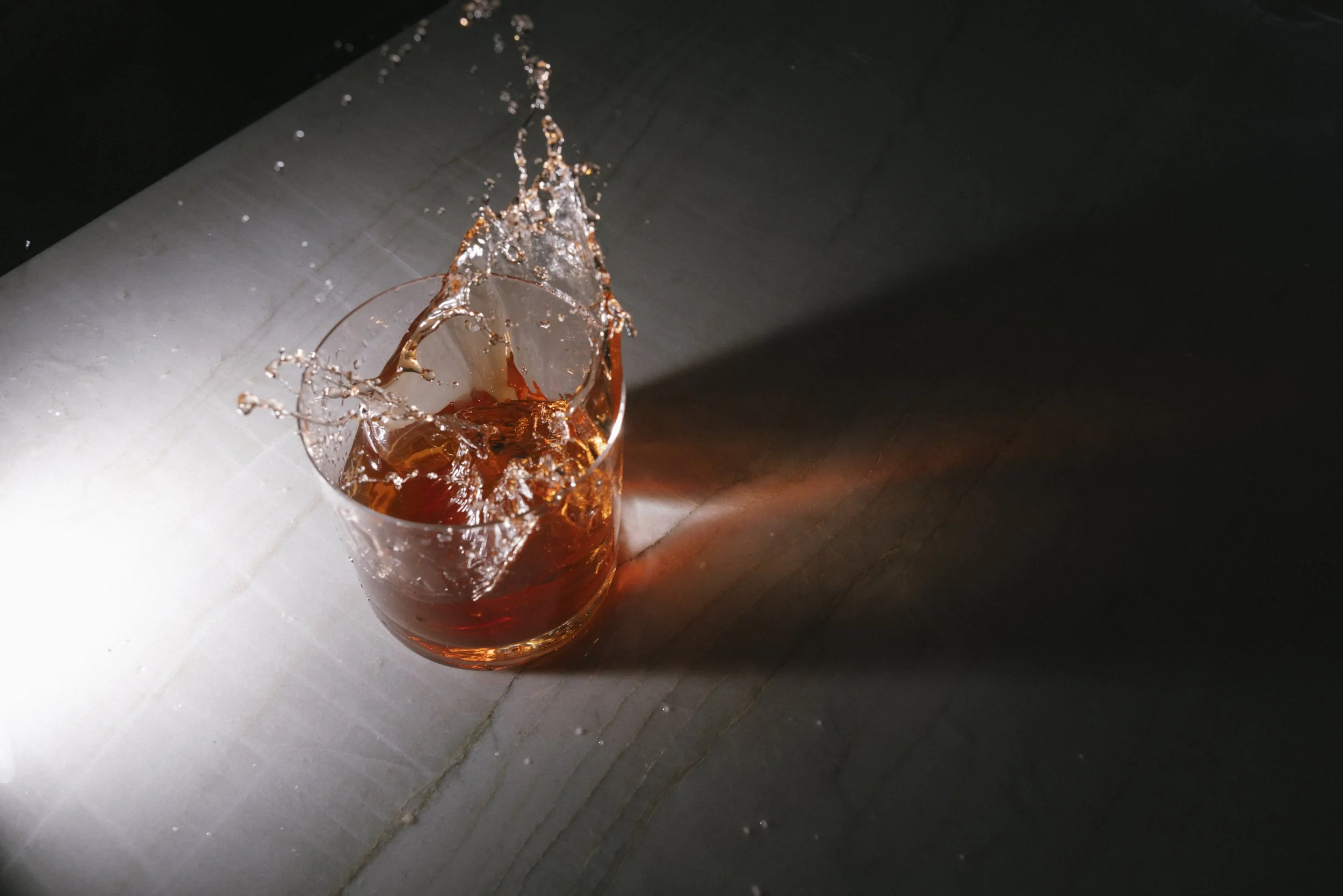 A glass with a dark reddish-brown drink being filled, causing a splash and splatter of liquid.