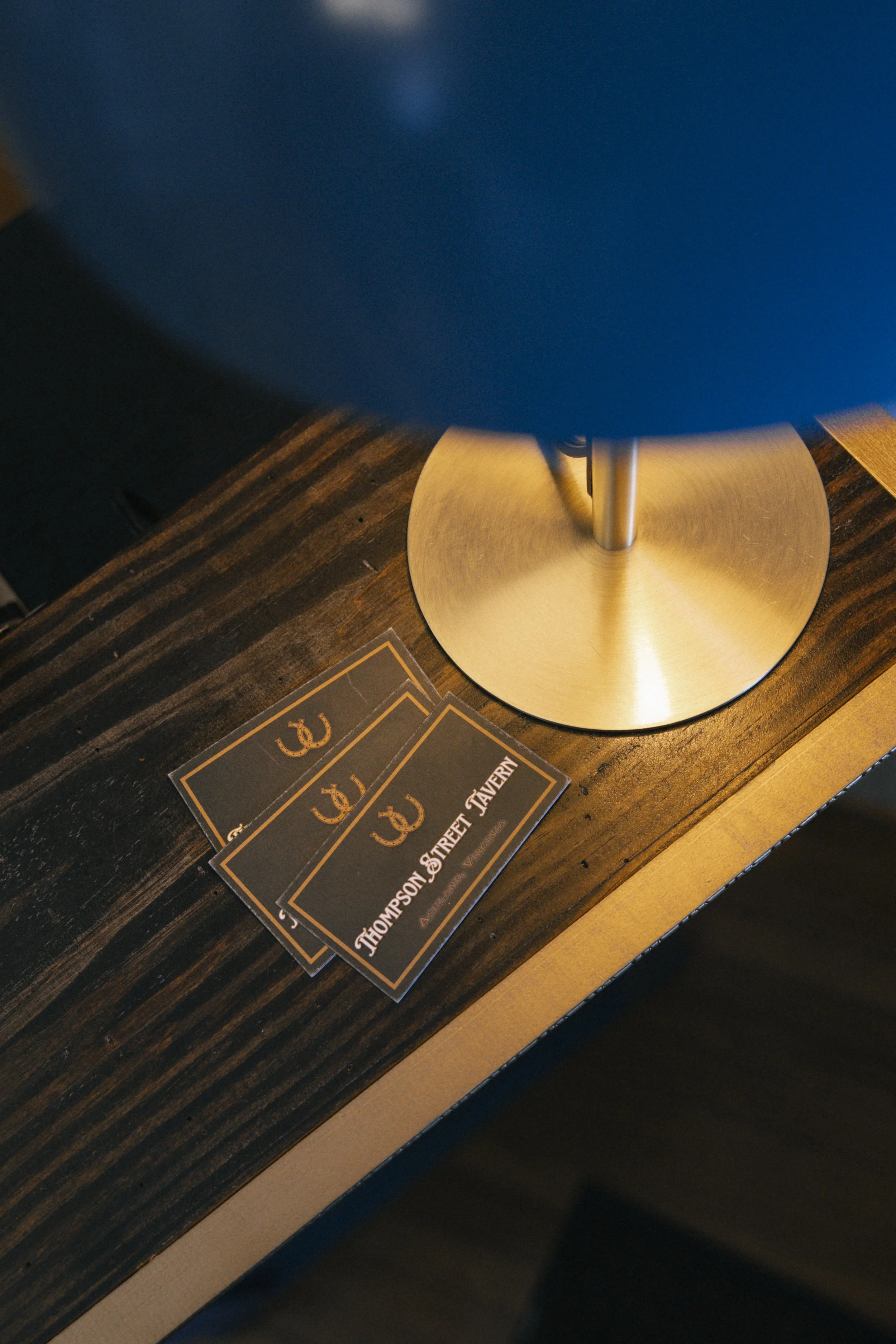 Table with a brass lamp and two cards on it, with a dark wooden surface and some printed text visible.