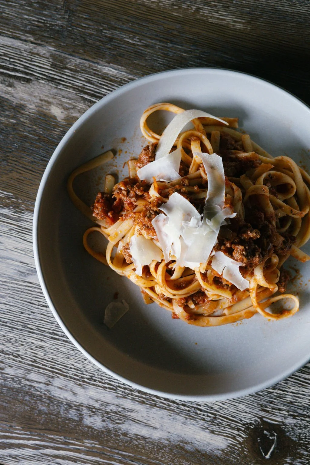 A plate of spaghetti with meat sauce topped with cheese on a rustic wooden table.