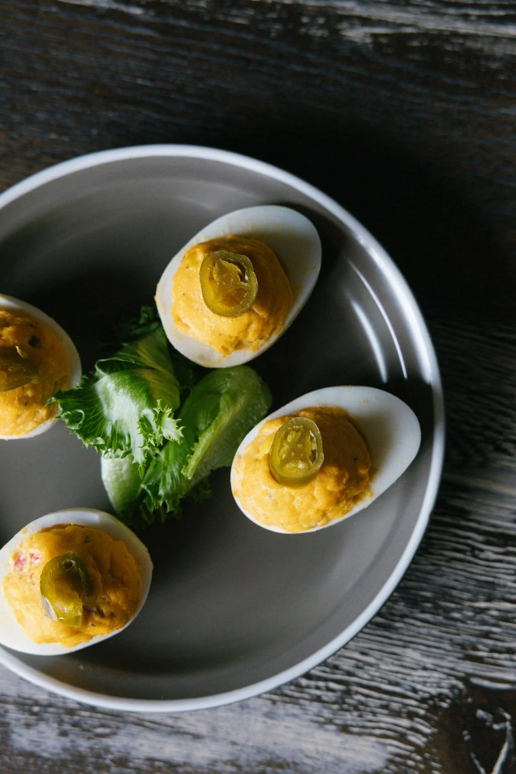 Deviled eggs topped with jalapeño slices, garnished with lettuce and lime wedge on a white plate.