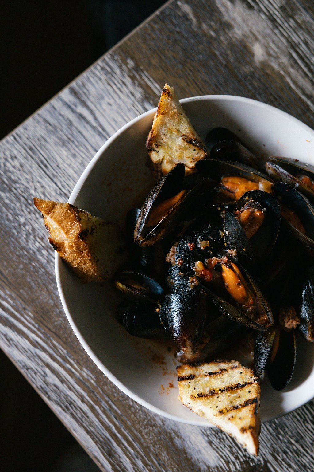 A bowl of mussels with grilled bread on a rustic wooden table.