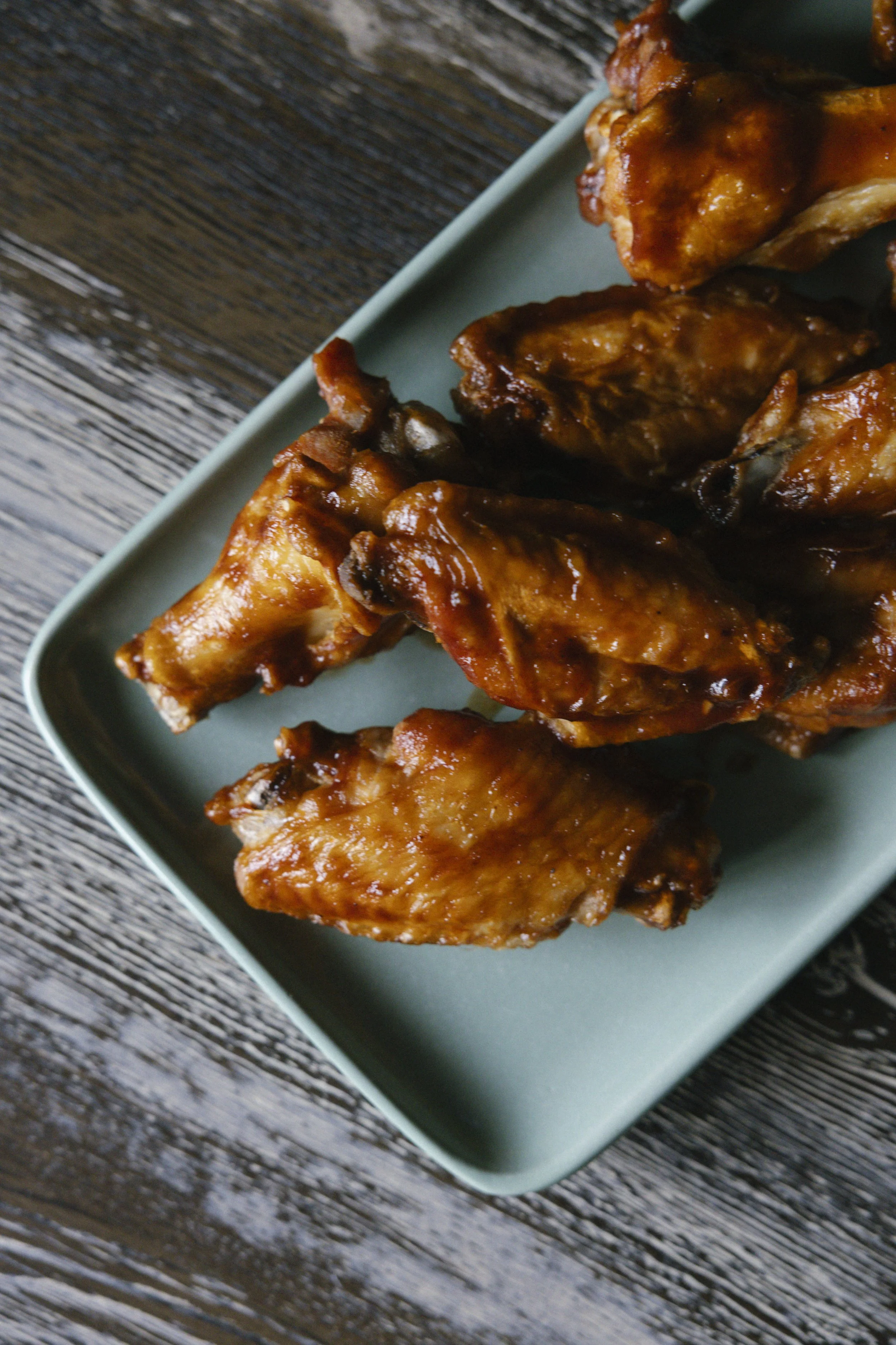 Barbecue chicken wings on a rectangular teal plate sitting on a weathered wooden surface.