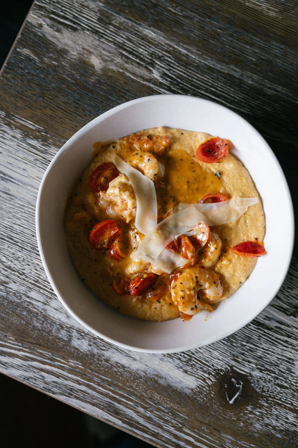 Bowls of creamy shrimp and cherry tomato dish garnished with white cheese and black pepper, served on a rustic wooden table.