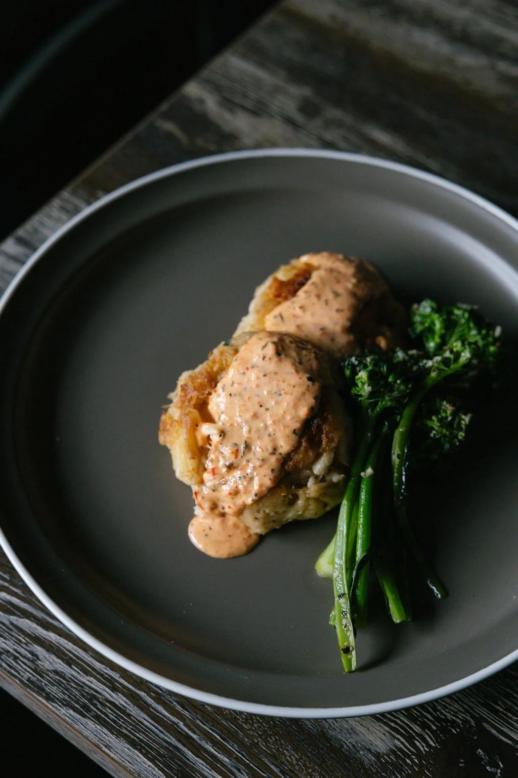 A plate with two pieces of stuffed chicken breast topped with a creamy sauce, accompanied by cooked broccoli.
