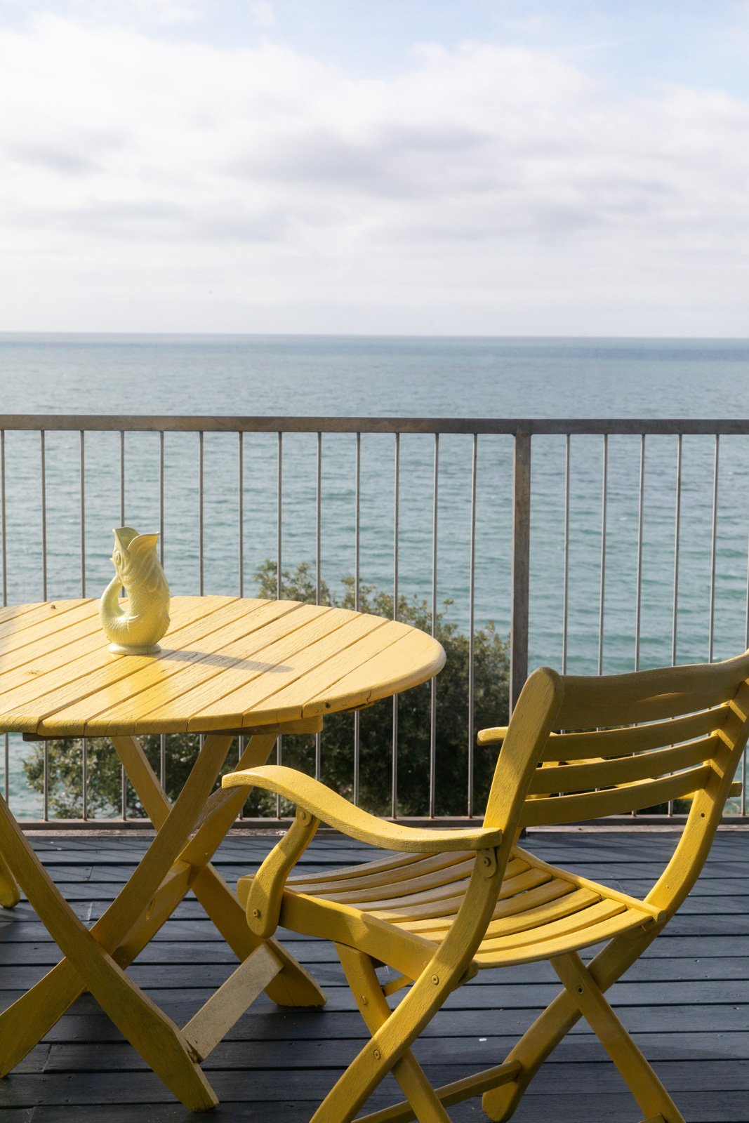 Yellow outdoor table and chair set on a balcony overlooking the English Channel with cloudy sky.