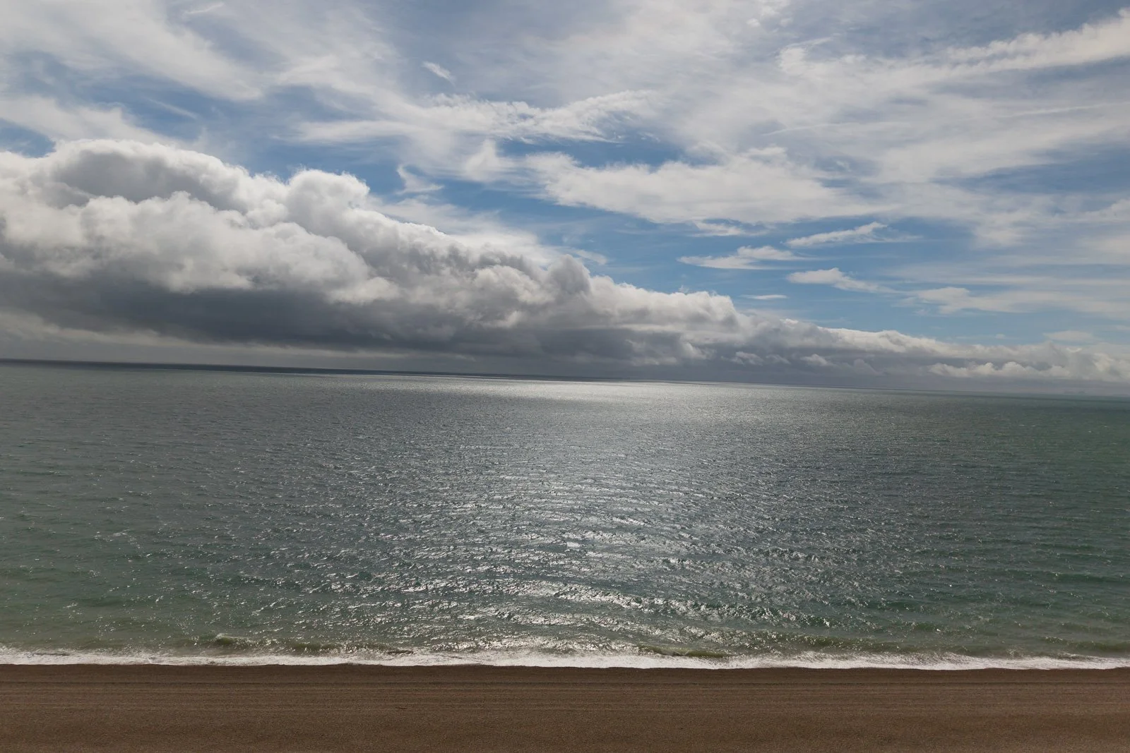 Cloudy sky over a calm ocean with a strip of sandy beach in the foreground.