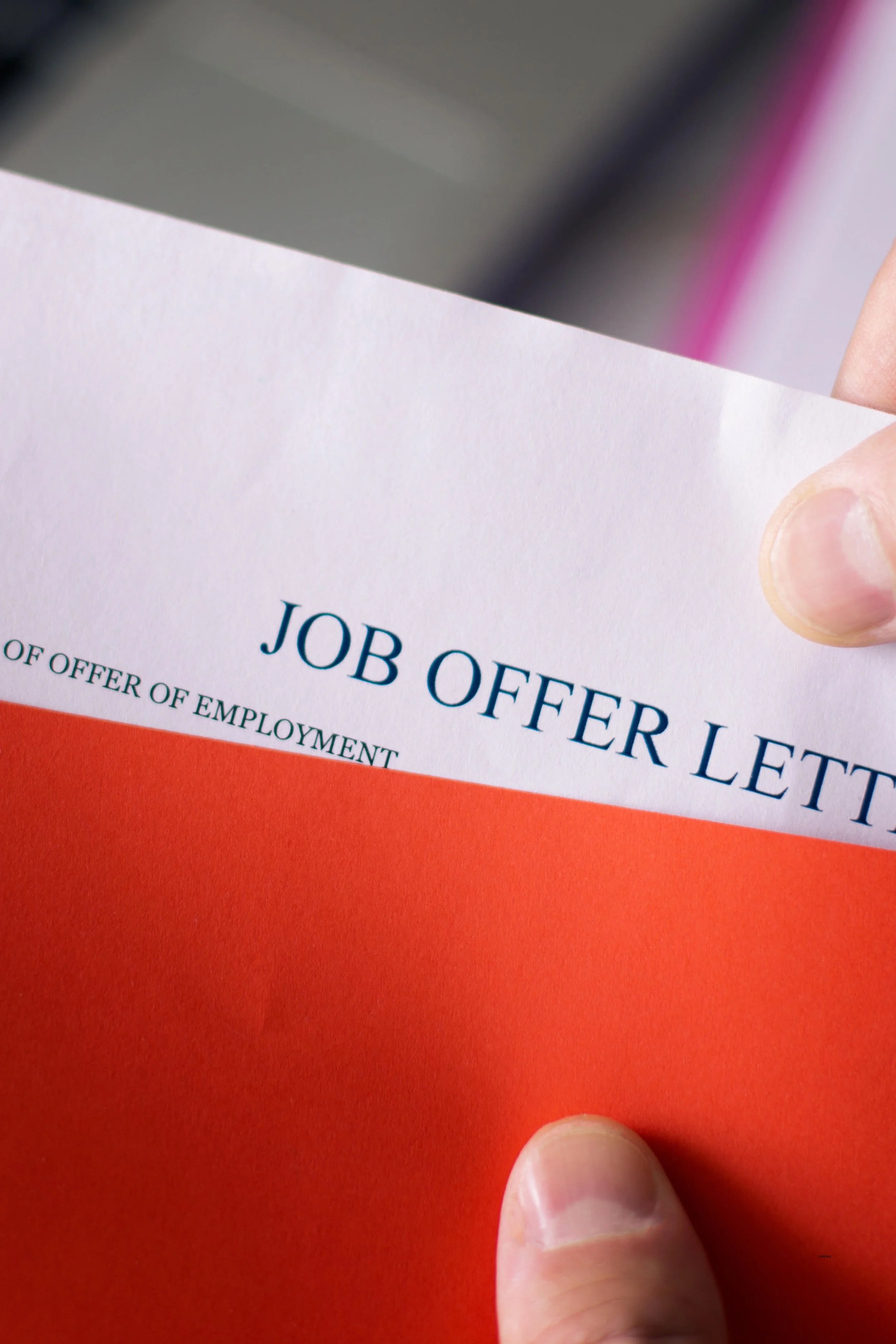 Close-up of a hand holding a job offer letter with employment-related text