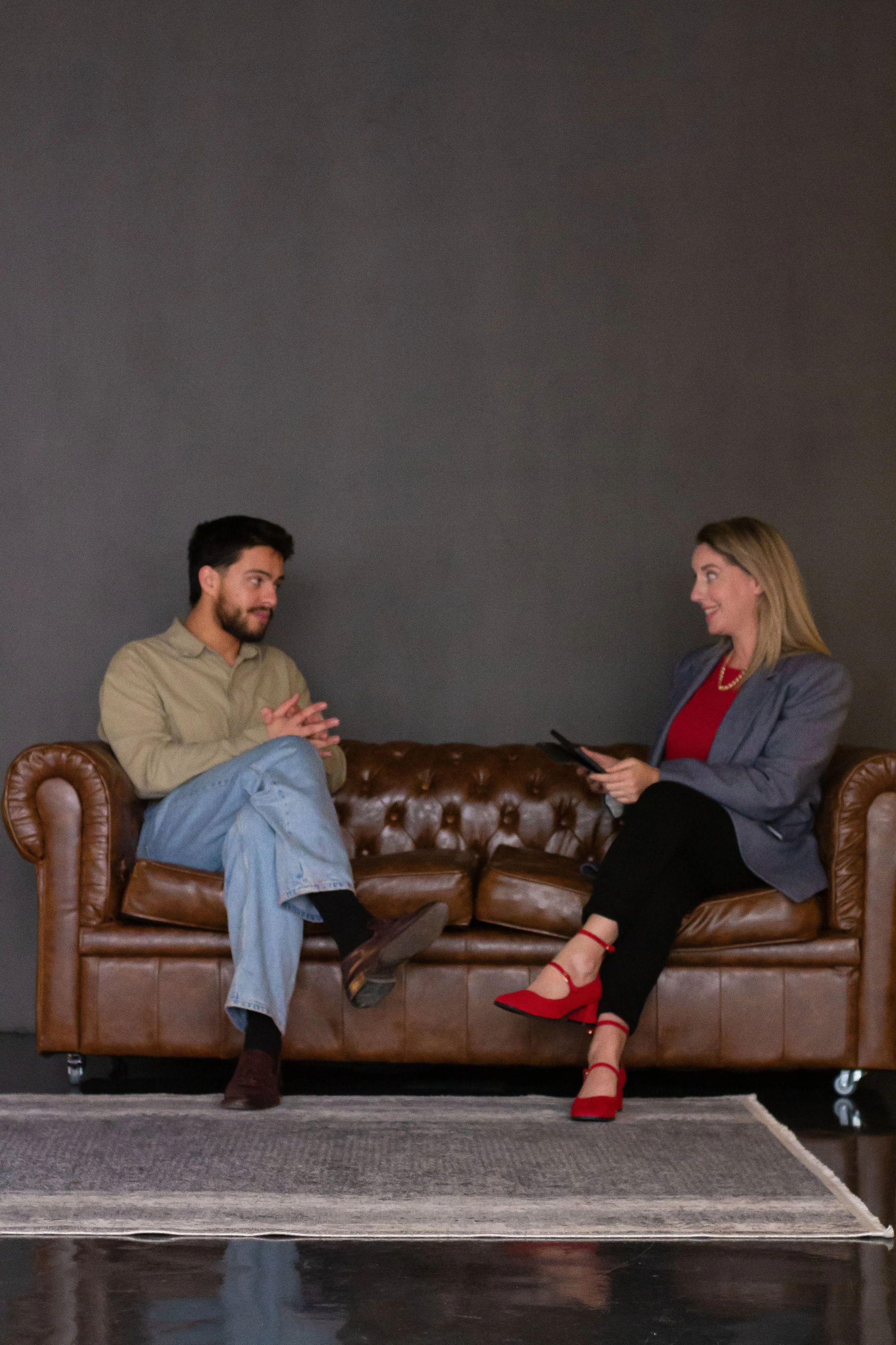 Man and woman talking while seated on a brown leather couch