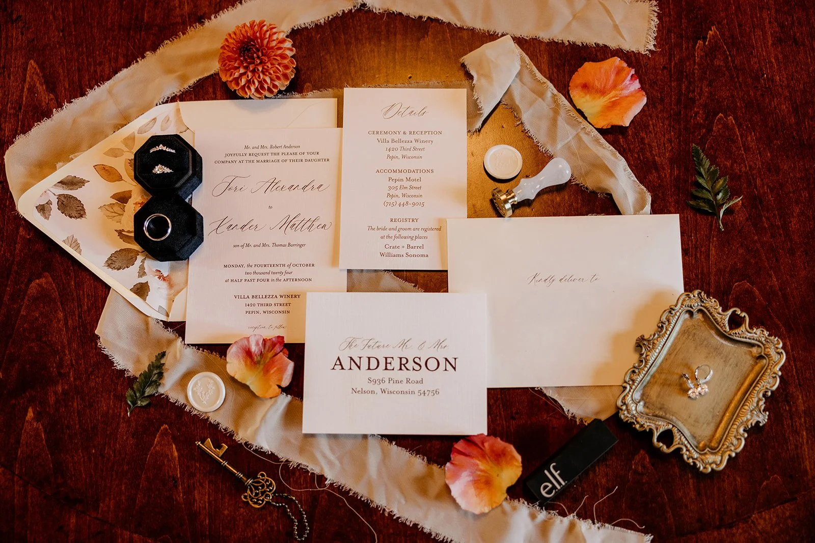 Wedding invitation suite with rings, jewelry, and decorative flowers on a wooden surface.