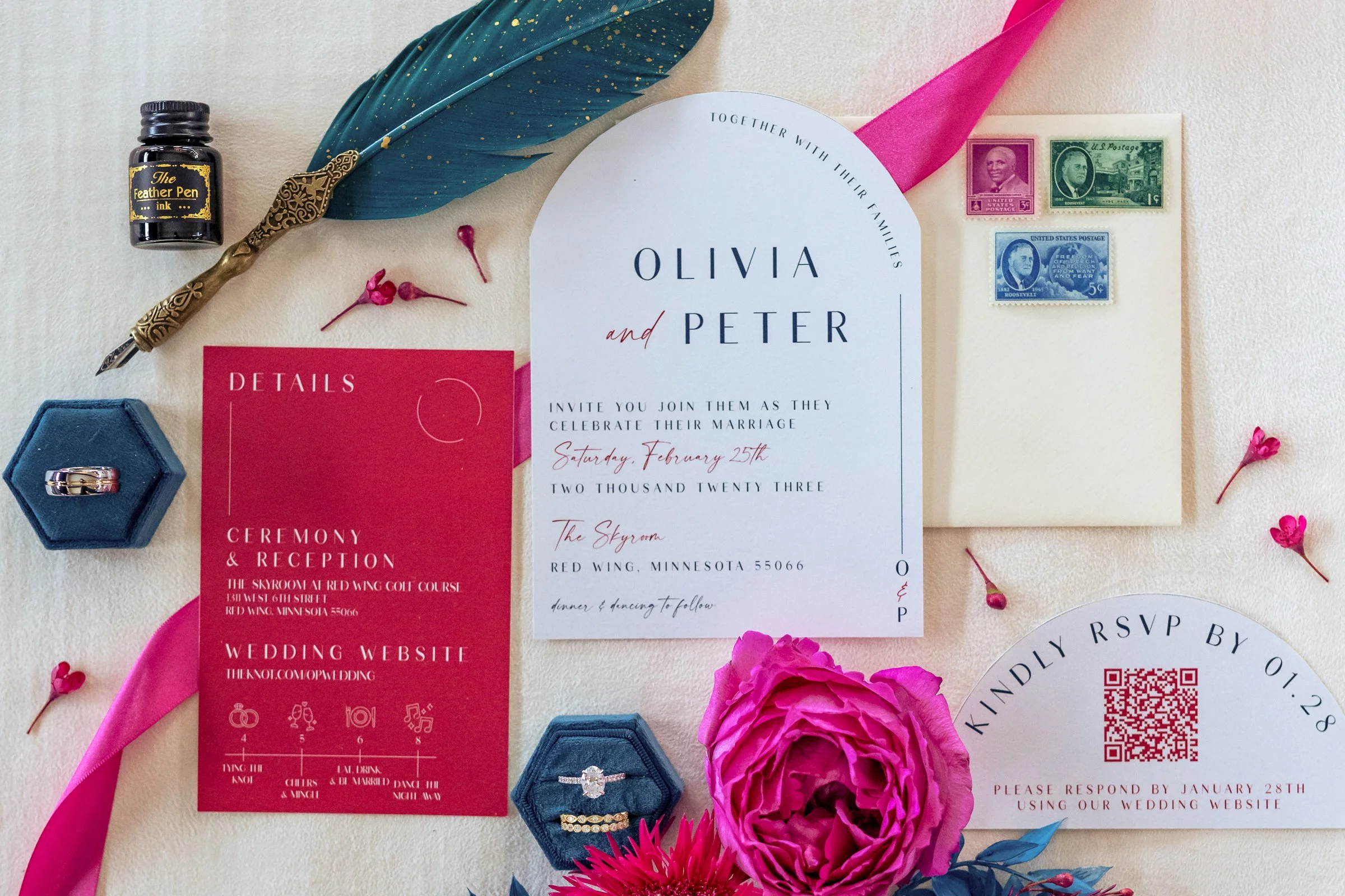 Wedding invitation suite with bride and groom's names Olivia and Peter, wedding details, RSVP card, pink flower, blue and pink stationery, postage stamps, a ring in a blue box, a bottle of ink, a feather quill, and scattered pink flower petals.