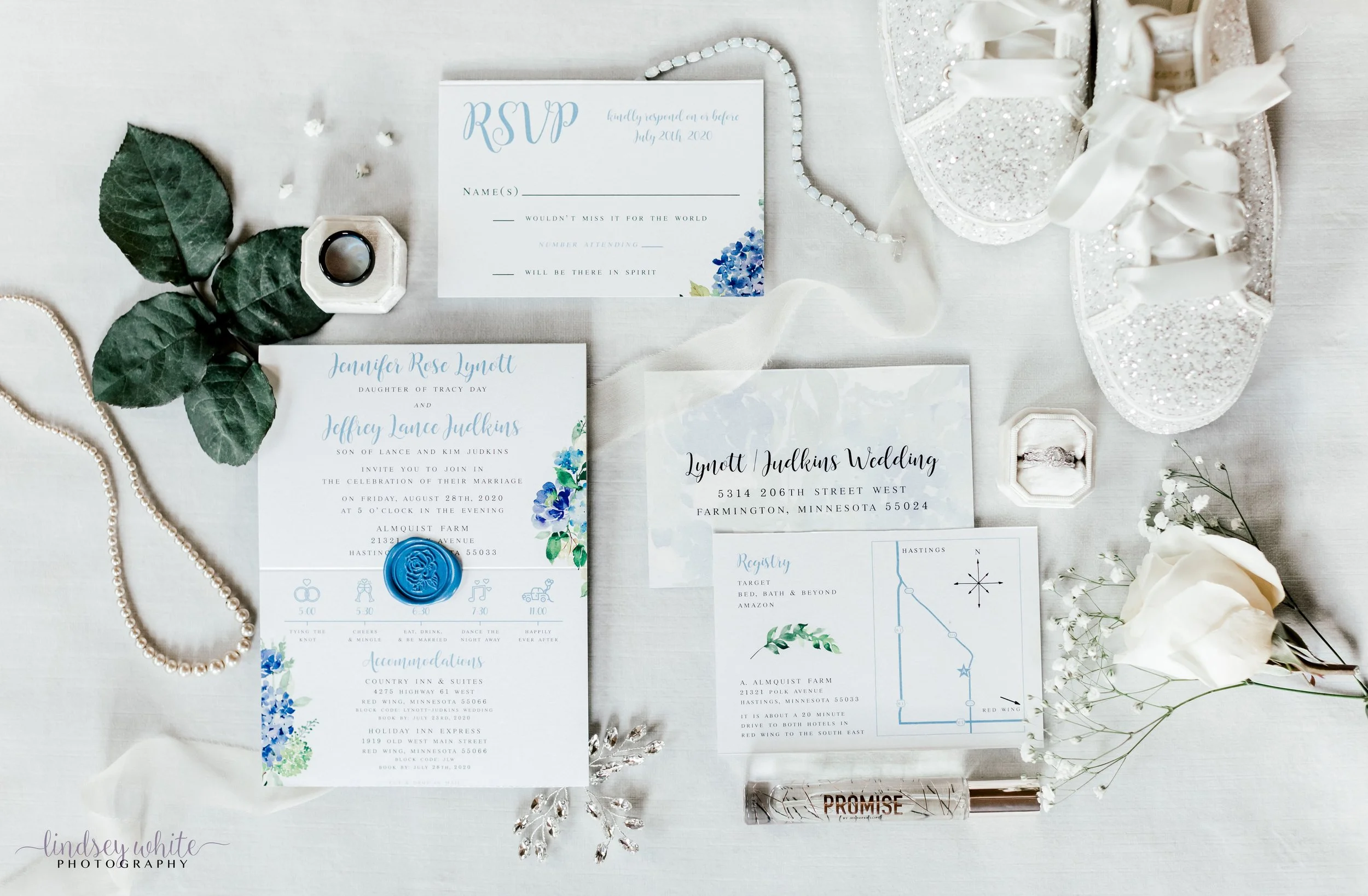 Wedding invitation suite with RSVP card, map, and details, surrounded by flowers, jewelry, and decorative items on a light surface.
