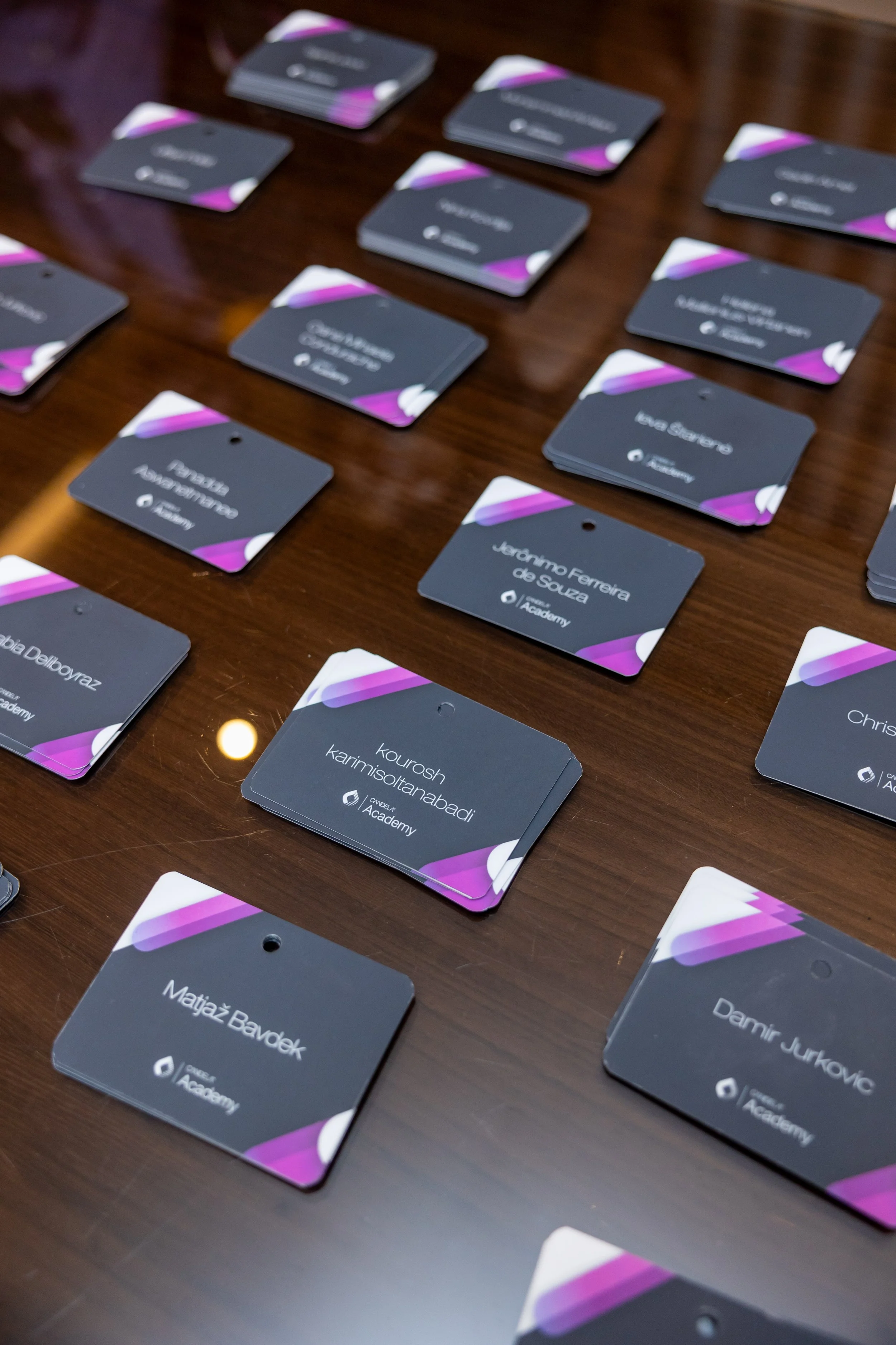 Multiple identification badges with names and logos of Academy, laid out on a wooden table.