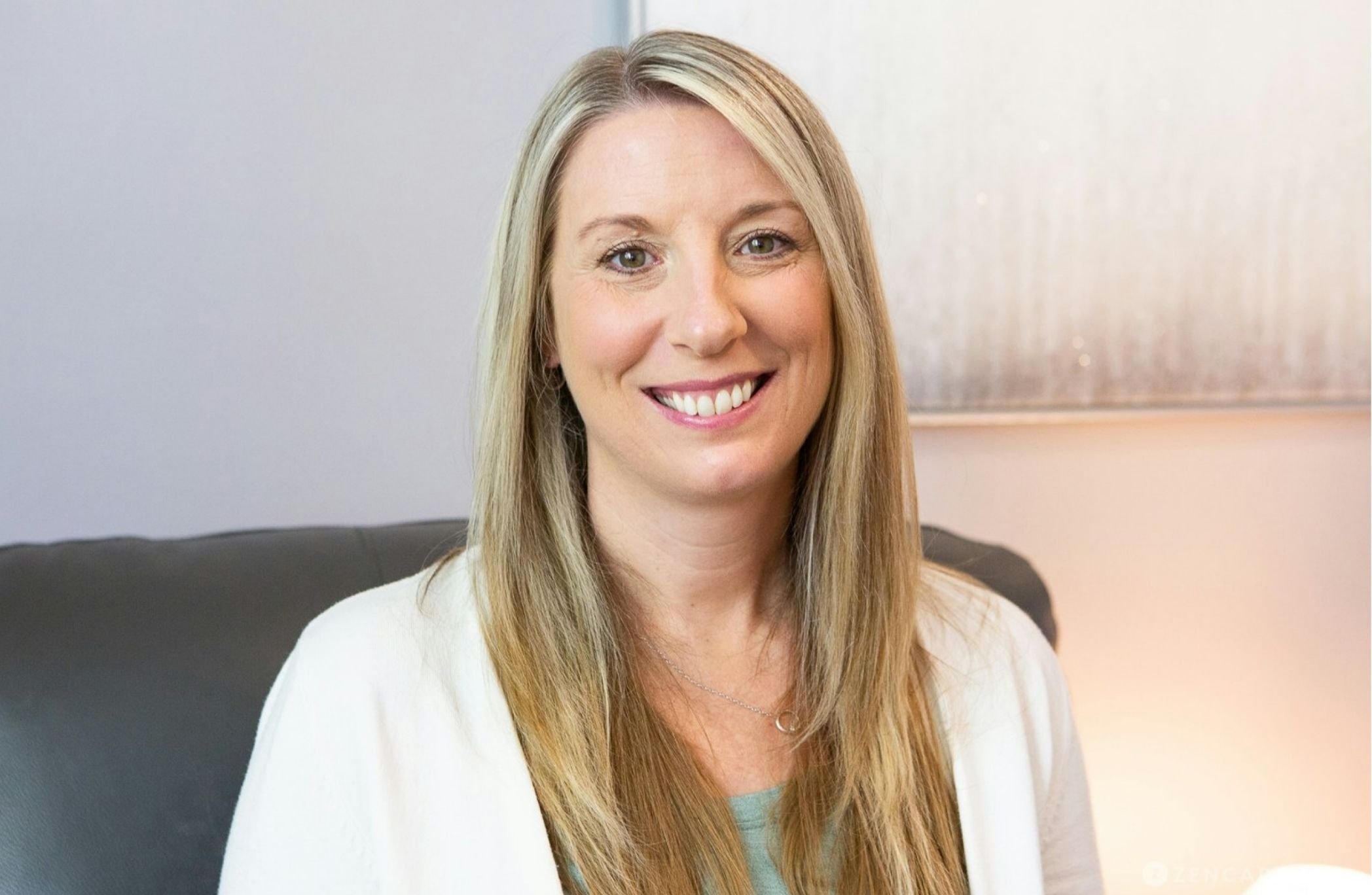 Cadence Chiasson, a certified EMDR therapist in Morrison, CO, with long blonde hair and green eyes, smiling while sitting in front of a light-colored wall and a black couch.