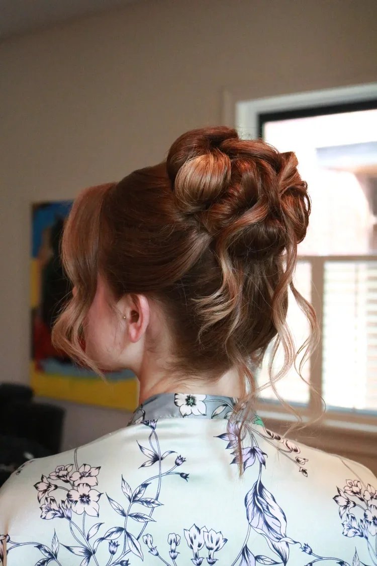 Woman with styled curly updo hair wearing a floral-patterned garment in front of a window.