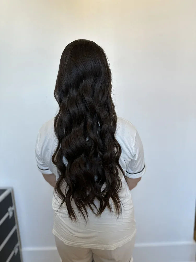 Back view of a woman with long, dark, wavy hair wearing a white shirt.