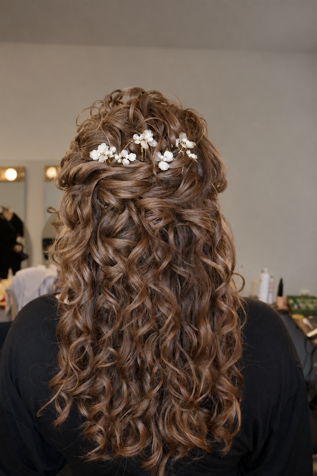 Back of a woman with long, curly brown hair decorated with white floral hair accessories.