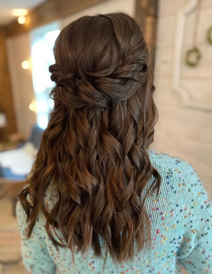 Back view of a woman with medium-length, wavy brown hair styled in a half-up, half-down hairstyle.