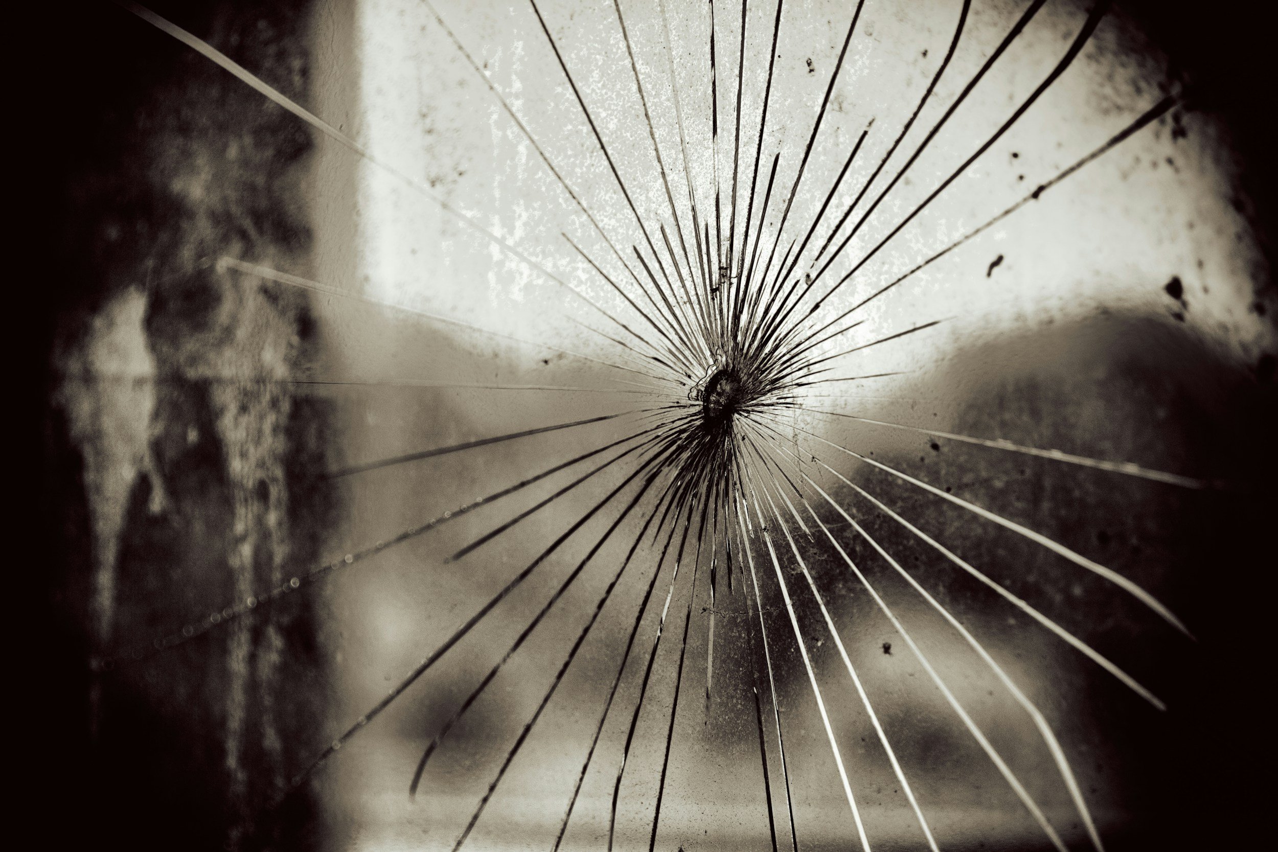Close-up of a shattered glass surface with spiderweb cracks radiating from a central point.