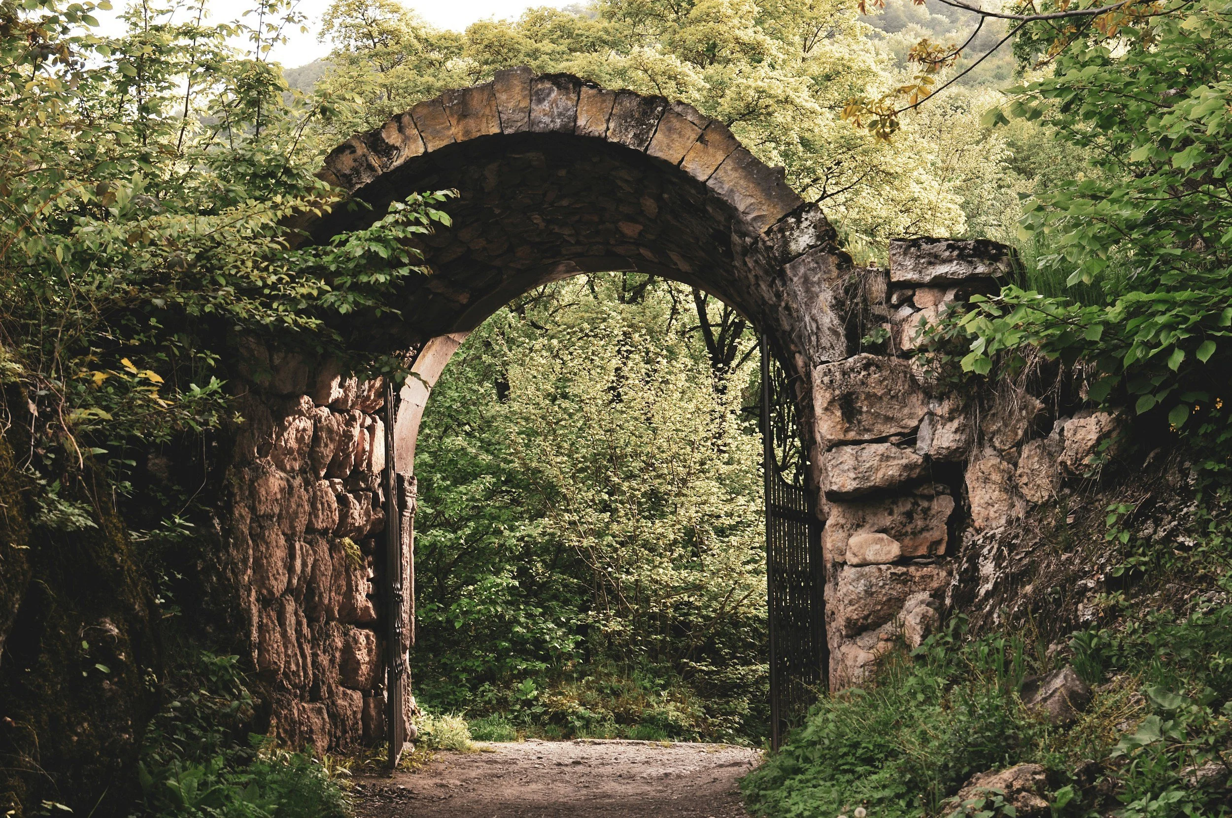 A stone archway surrounded by green foliage and trees in a forest setting.