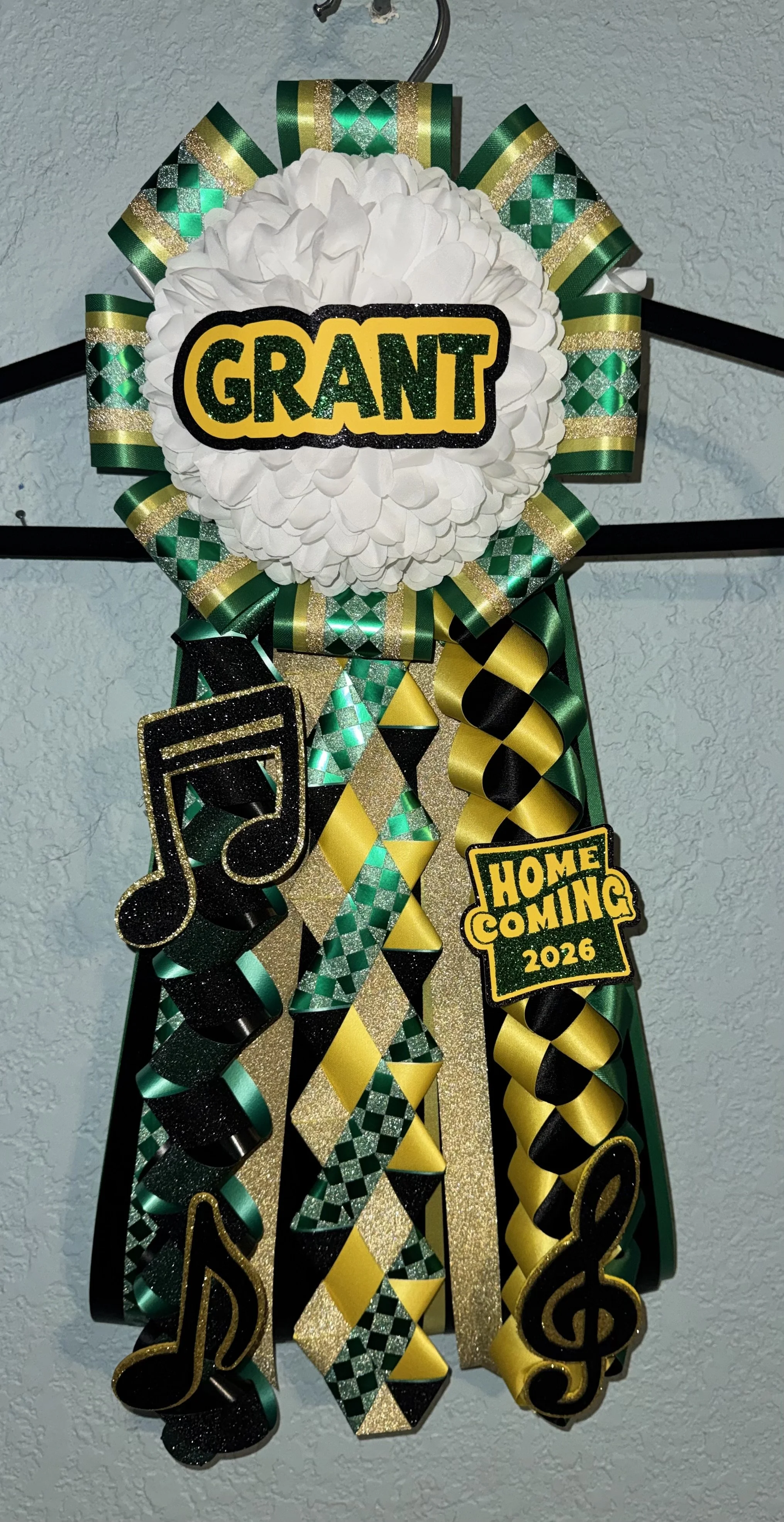 Decorative door wreath for Grant's homecoming event, featuring white flowers, green, yellow, and black ribbons, musical note and 'Home Coming 2026' signs.