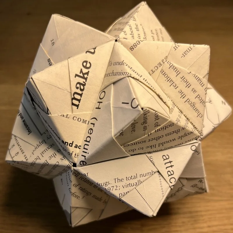 An origami polyhedron made out of folded book pages on a wooden surface.