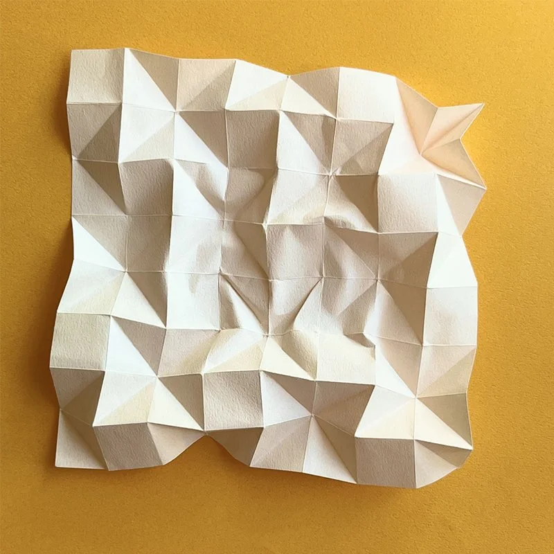 A crumpled sheet of white paper with folded geometric patterns on a yellow background.