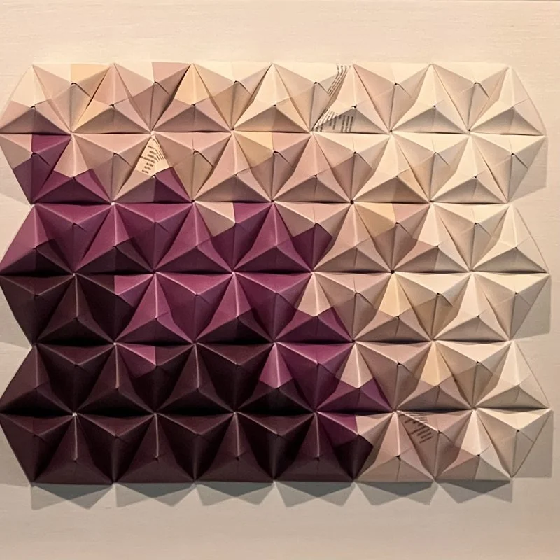 Arrangement of paper pyramids in shades of beige, pink, and purple on a white surface.