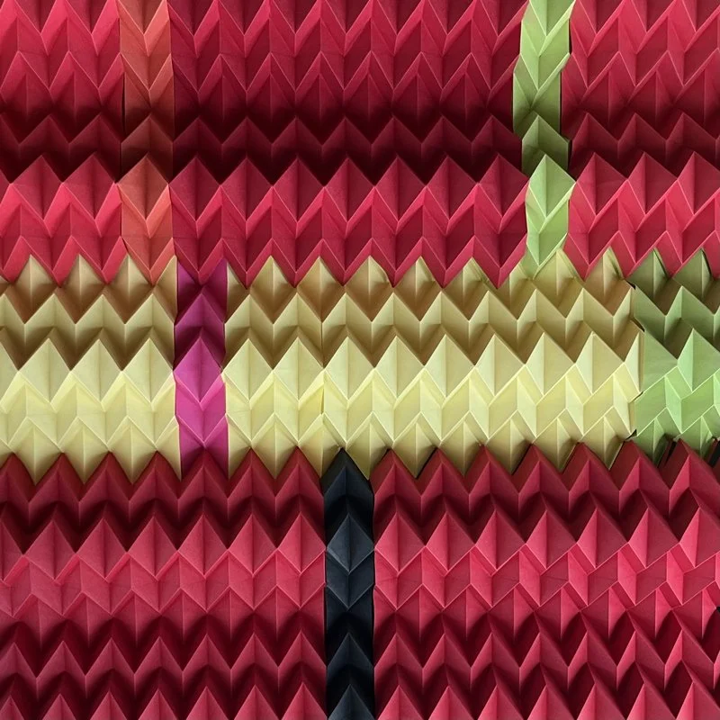 Colorful geometric paper art in chevron pattern with shades of pink, red, yellow, black, and green.