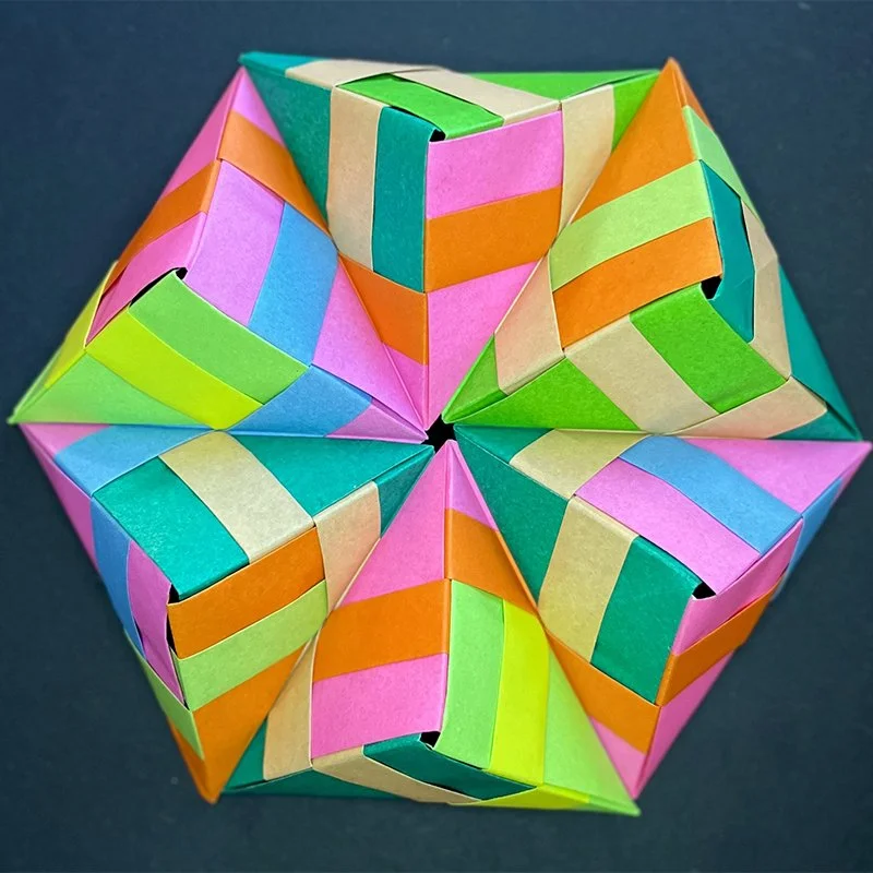Colorful origami paper-folded star with multiple geometric shapes, vibrant colors including pink, orange, green, blue, and beige, on a dark background.