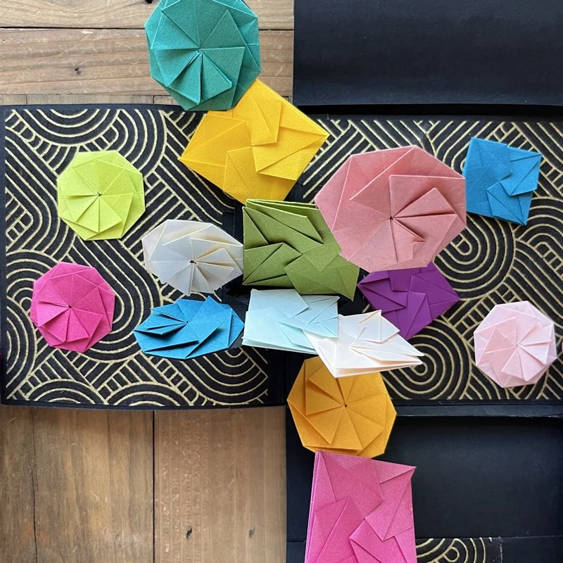 A pop-up of colorful origami paper octagon twist and tato envelopes on a black patterned surface.