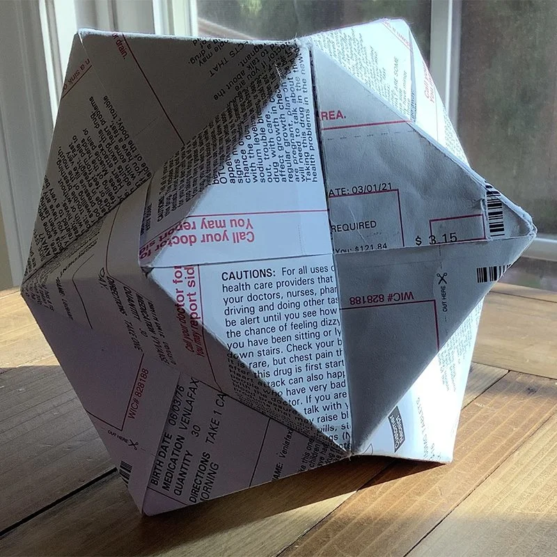 A 3d paper solid made from folded prescription receipts, placed on a wooden table near a window.